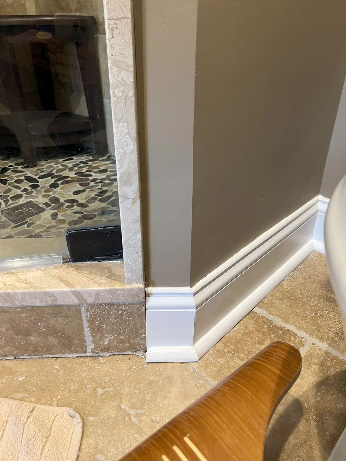 After: clean new white baseboard trim installed against the same stone tile floor